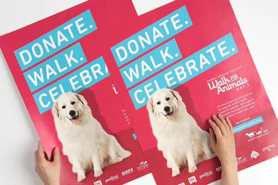 Two hands holding custom posters printed for an animal nonprofit with Donate. Walk. Celebrate. in white letters.