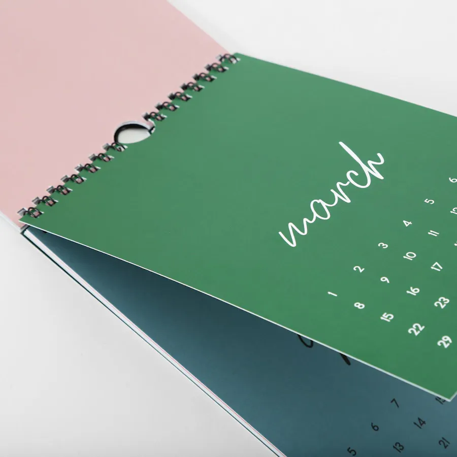 A personalized calendar printed with a black wire coil binding and pages in pink, green and blue.
