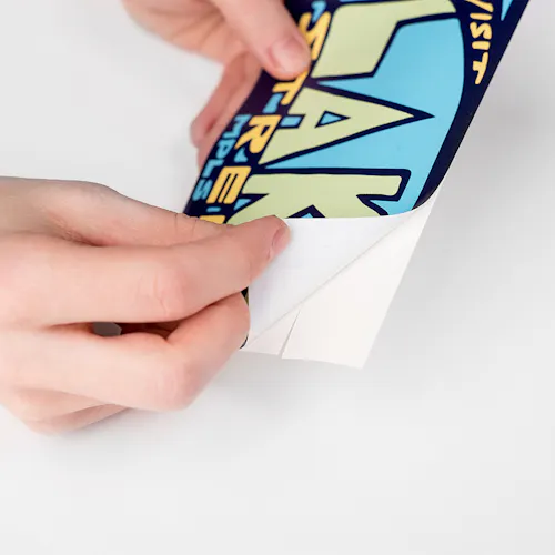 Two hands peeling a custom decal off its backing, printed with Visit Lake Street in blue, yellow and green.