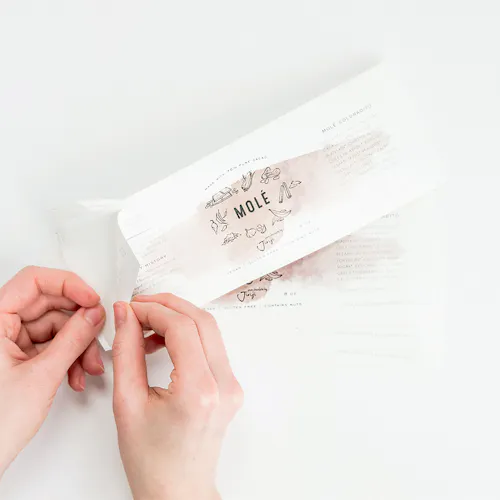 White Polypropylene - Removable, 9 x 3" Two hands peeling a product label off its backing, printed with Mole and graphics of vegetables in the middle.