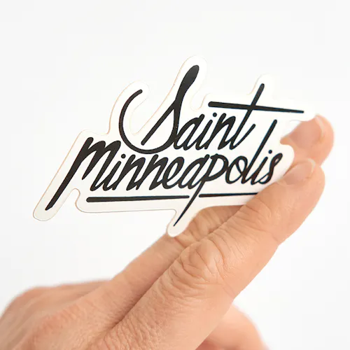 White Polypropylene - Permanent, 2.5 x 2.33, Die Cut Single A custom die-cut sticker printed with Saint Minneapolis in black held between two fingers.