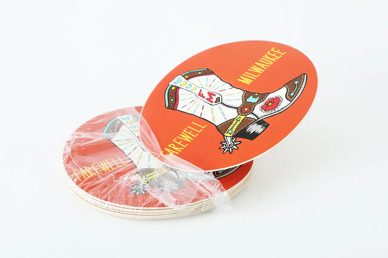 A stack of round stickers custom printed with an orange background, cowboy boot and Farewell Milwaukee in yellow.