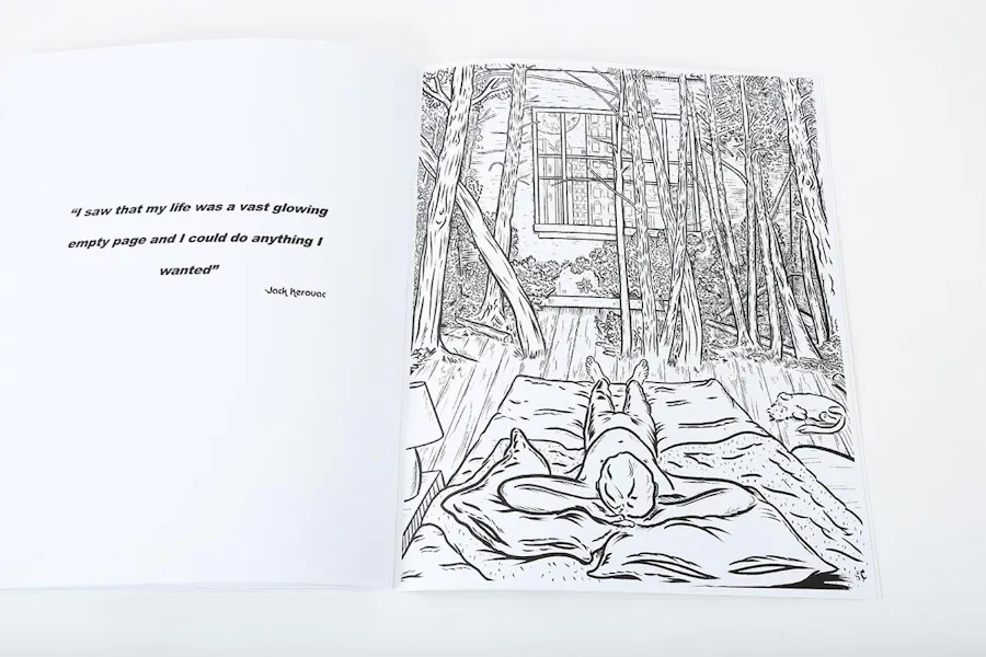 A custom coloring book laying open to a black and white cabin illustration and a Jack Kerouac quote.
