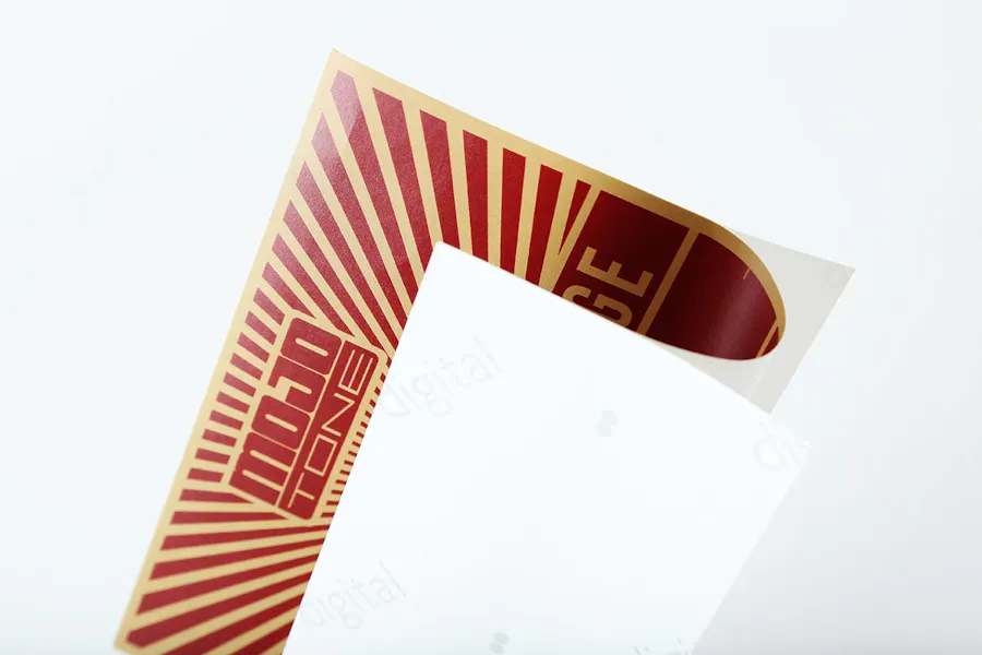 A custom packaging label with a red and gold design and the white backing peeling off.