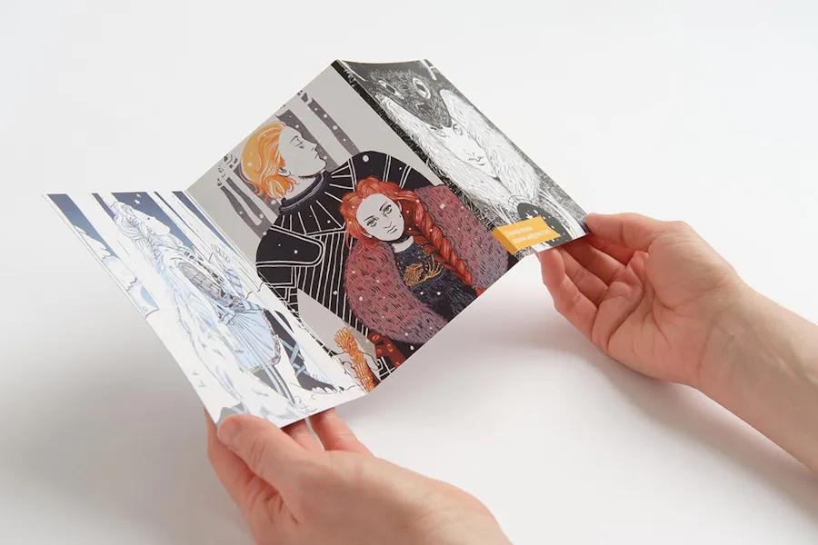 Two hands holding an unfolded brochure printed with custom fantasy graphics and artwork.