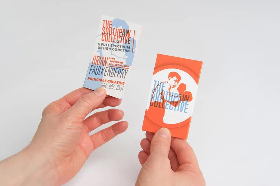 Two hands holding two custom business cards with a vertical orientation and an orange, blue and white design.