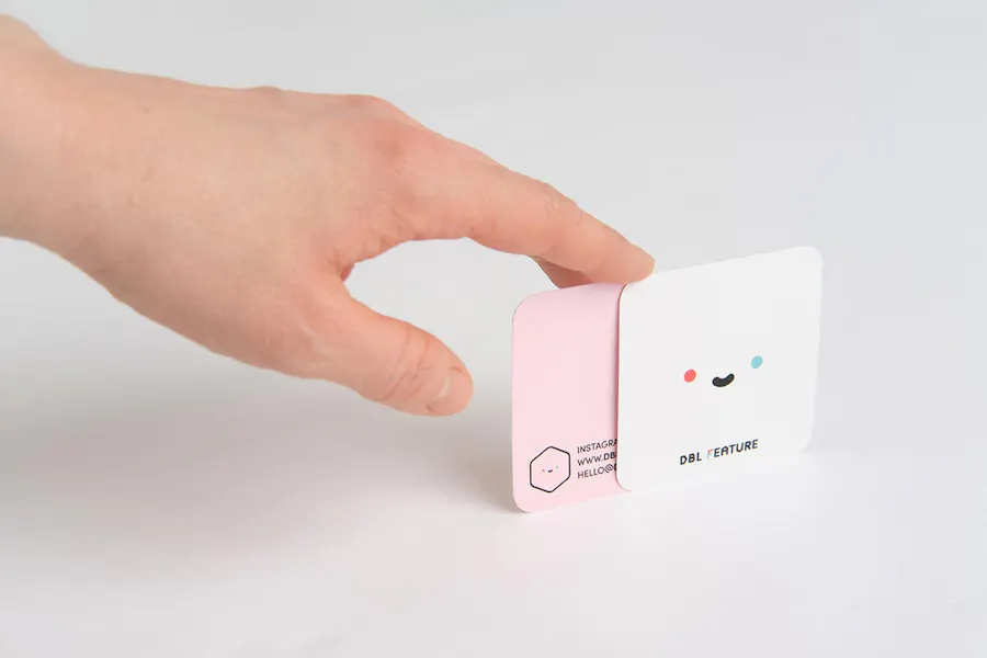 A hand holding two square business cards with a white front and a pink back.