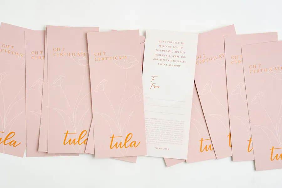 Custom rack cards designed as gift certificates, with a light pink design and orange lettering.