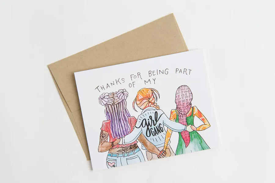 A custom card printed with a colorful drawing of three girls holding hands on the front and a brown envelope behind it.