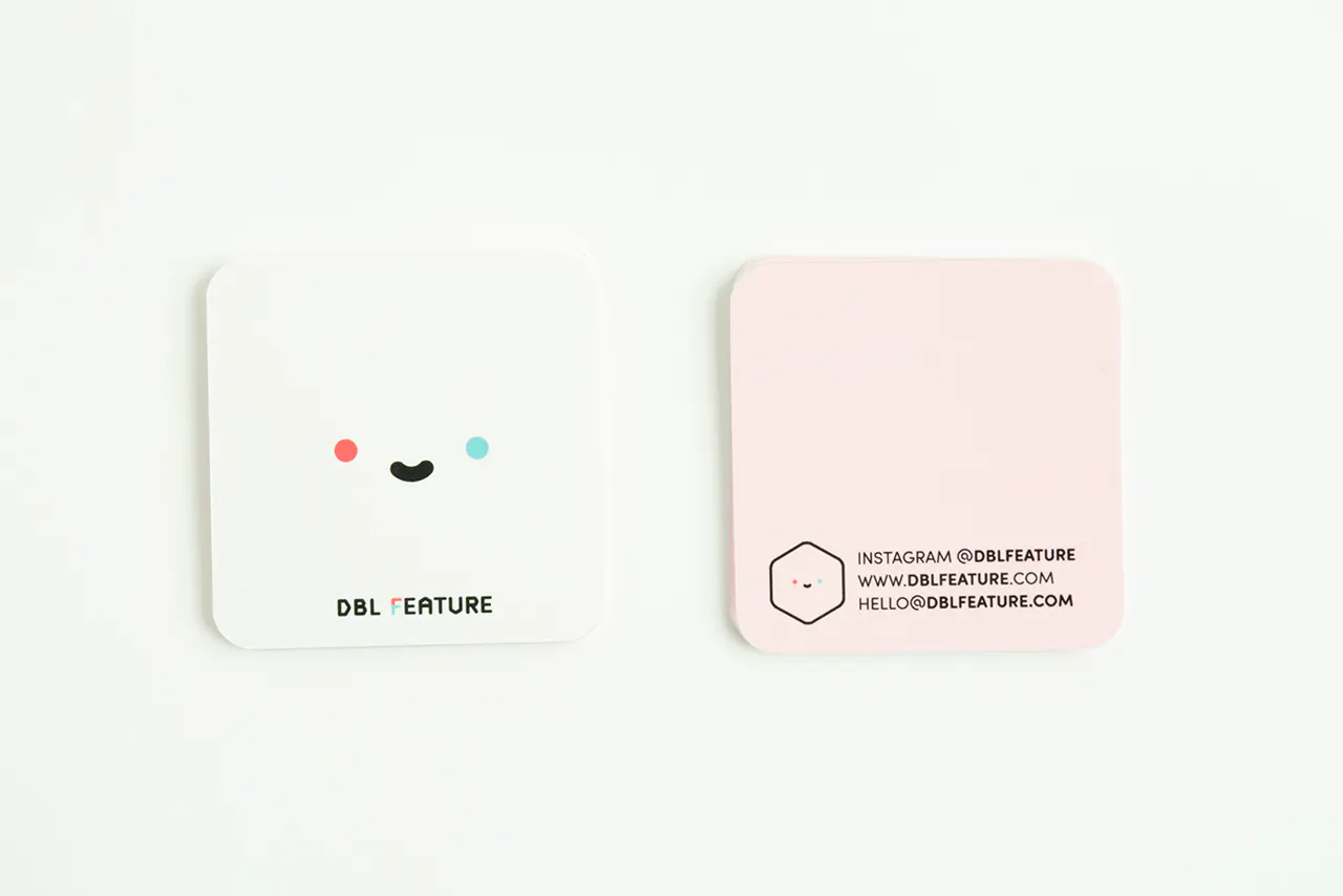 A unique business card with a square shape, a smiley face with a white background on the front and pale pink color on the back.