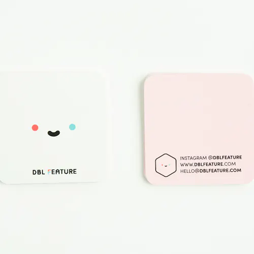 A unique business card with a square shape, a smiley face with a white background on the front and pale pink color on the back.