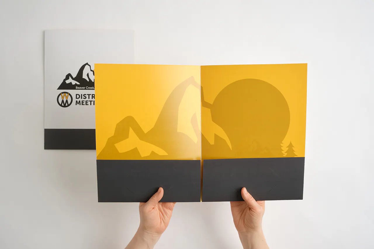 Two hands holding open a pocket folder with a black and yellow design.