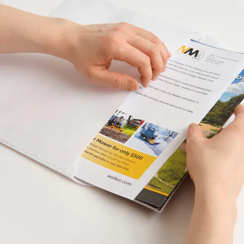Two hands inserting Walker Mower marketing materials into the side of a white envelope.