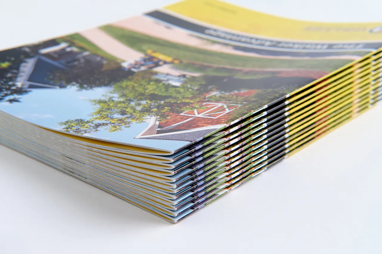 A stack of Walker Mower marketing booklets with a saddle stitch binding a man on a riding mower on the cover.