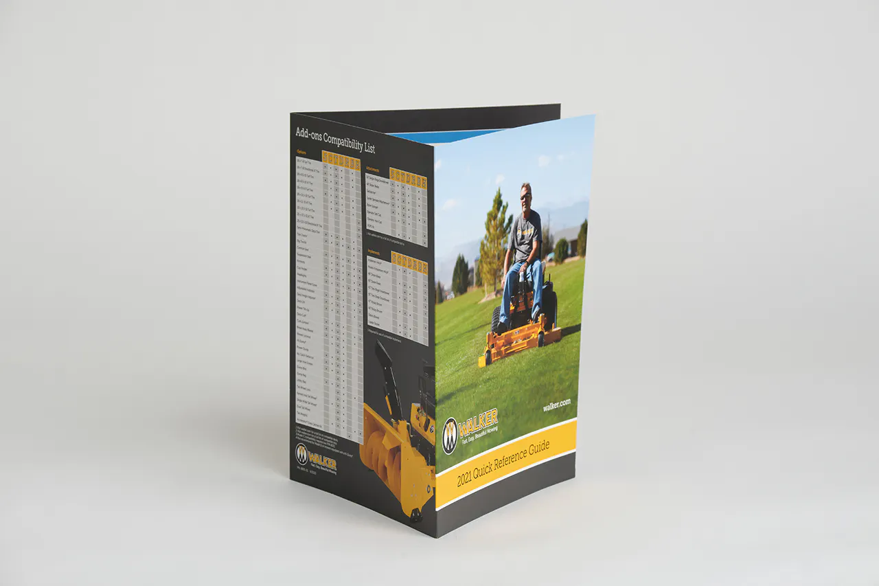 A Walker Mower product brochure standing open with a man on a riding mower on the front and a comparison list on the back.