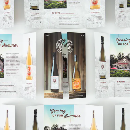 A custom brochure with a gate fold and images of wine bottles surrounded by more unfolded brochures with wine information.