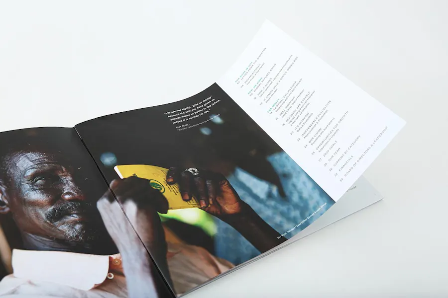 A nonprofit annual report laying open to an image of a man holding a yellow booklet and a table on content.