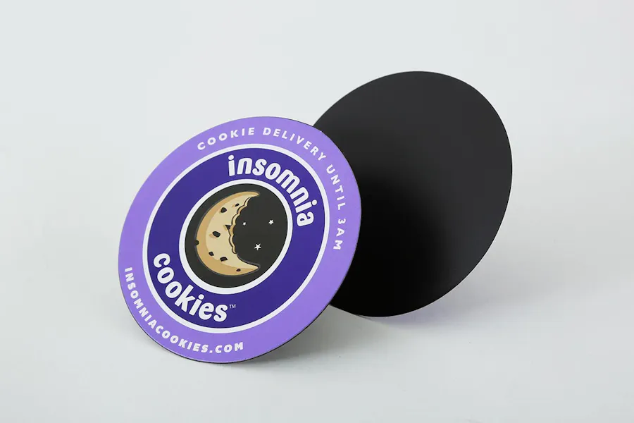 Two custom magnets printed with a round shape, purple design and Insomnia Cookies in white text.