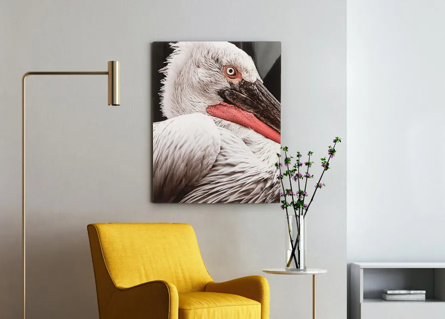 A metal print of a white bird hanging on a wall next to a yellow chair, side table and lamp.
