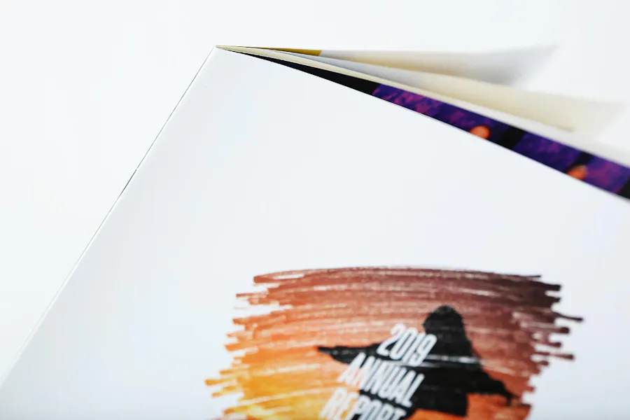 An annual report printed with a saddle stitch binding and a white cover with ombre artwork in red, orange and yellow.