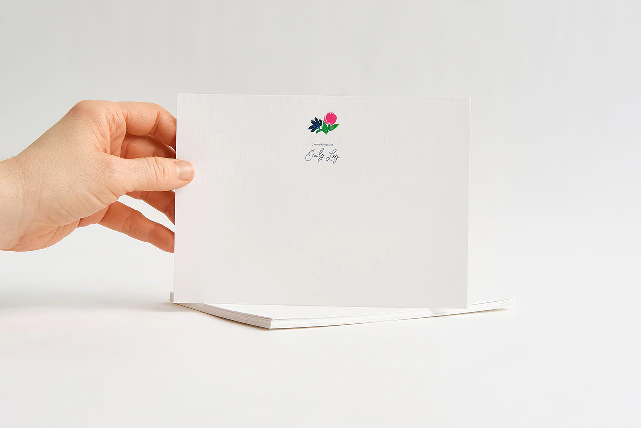 A hand holding a piece of custom stationery printed with From the Desk of Emily Ley and a floral design.