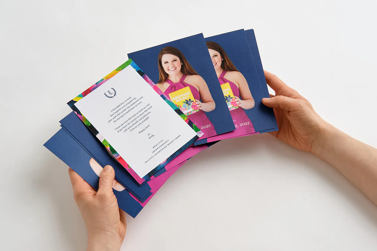 Two hands holding fanned-out postcards printed with a woman in a pink dress and a welcome note.