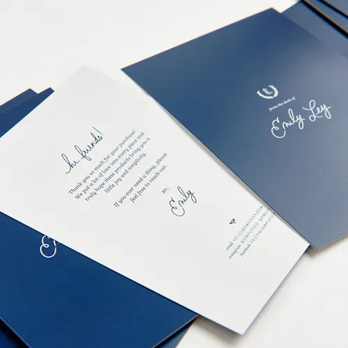 POSTCARD: 80# COATED MATTE WHITE COVER, 4 x 6" A stack of fanned-out package inserts printed with a navy blue design and a welcome note on the back.