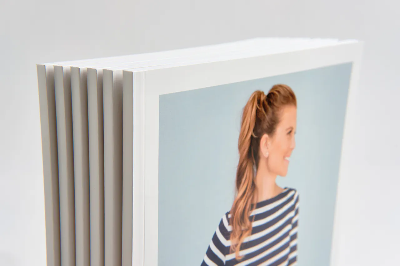 A stack of brand booklets standing with a woman in a striped top on the cover and a perfect binding.