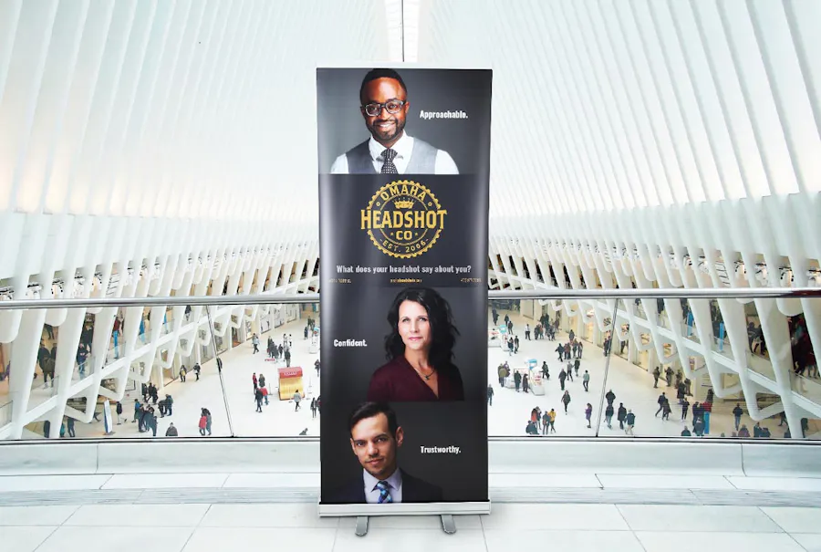 A retractable banner printed with Omaha Headshot Co. in yellow text and two men and a woman.