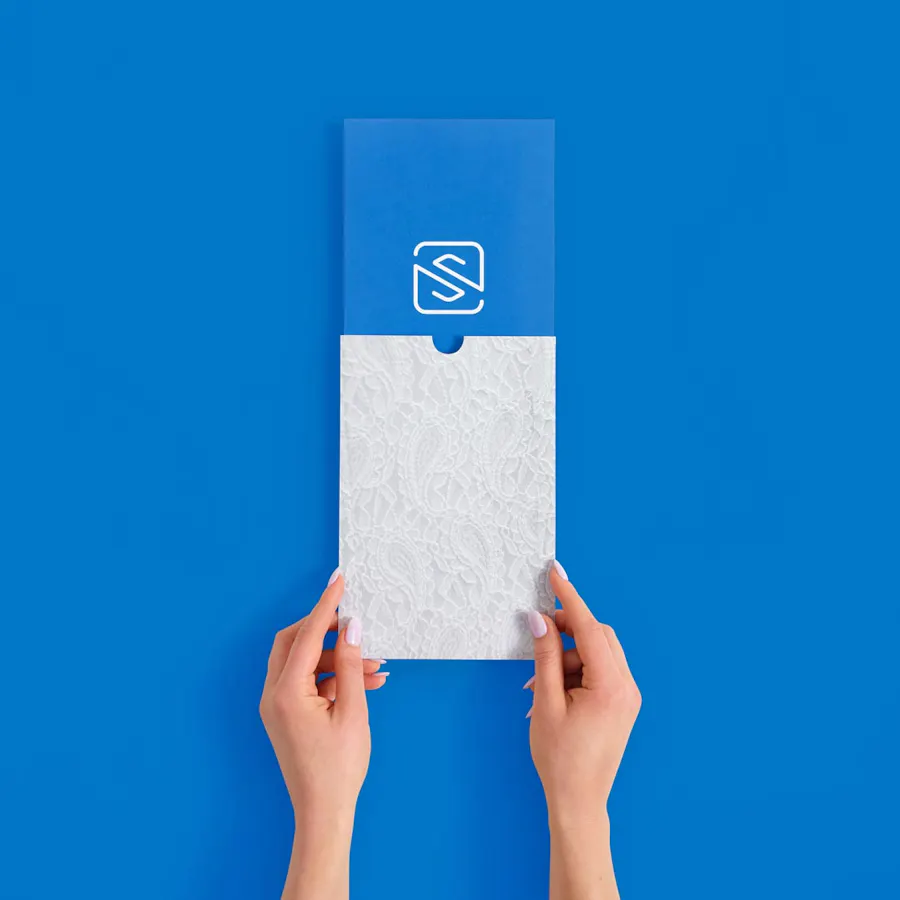 Two hands holding a white sleeve mailer with a lace paisley pattern and a blue insert card with the Smartpress logo.
