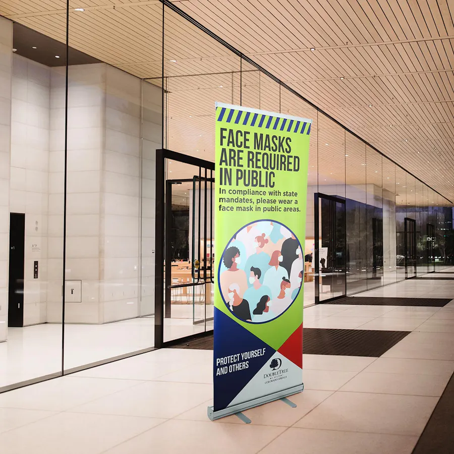 A retractable banner standing in a lobby with health and safety messaging and a green, blue and red design.
