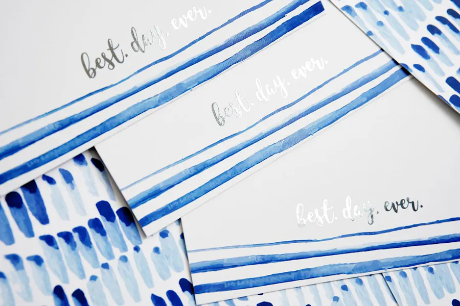Three custom invites with a blue design and silver foil printed with digital sleeking.