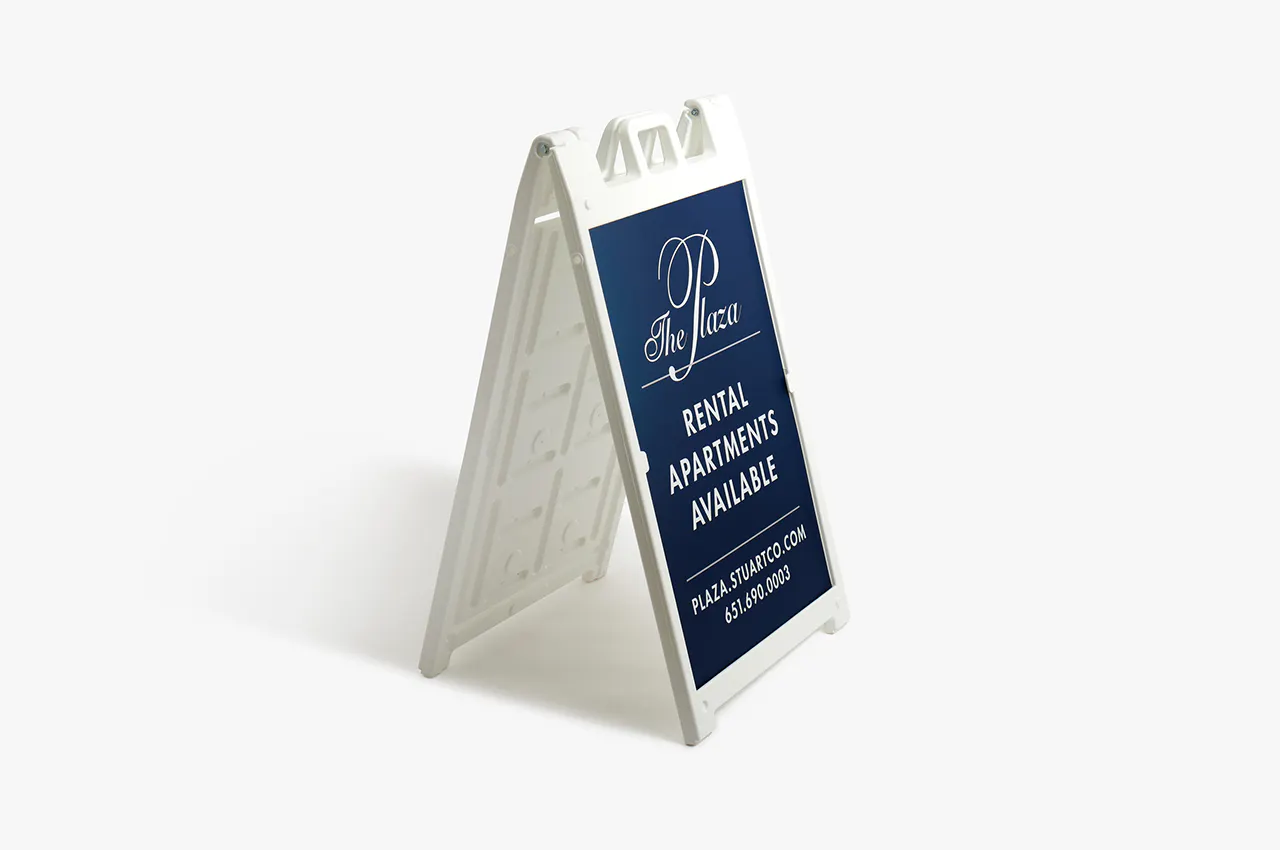 A white A-frame stand with a navy blue sign printed with The Plaza Rental Apartments Available in white.