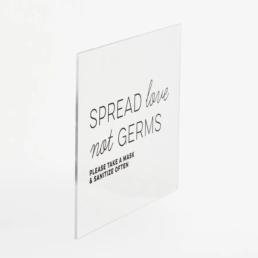 An acrylic sign that says "Spread Love Not Germs" in black letters.