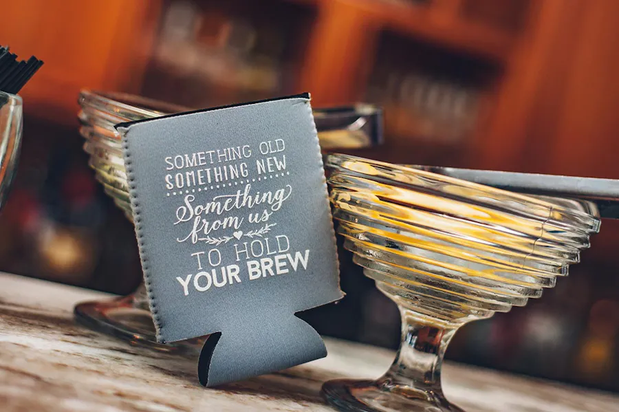 A custom can koozie wedding favor on a drinks table with Something from us to hold your brew.