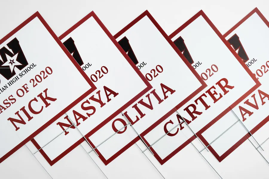 Five graduation yard signs printed with student names in a red, white and black design.