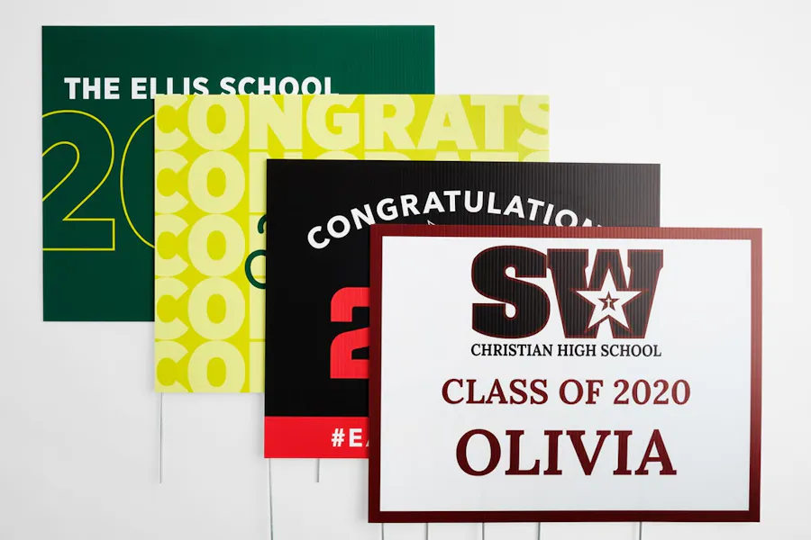 Four custom lawn signs overlapping each other with graduation designs in green, yellow, black and red for the class of 2020.