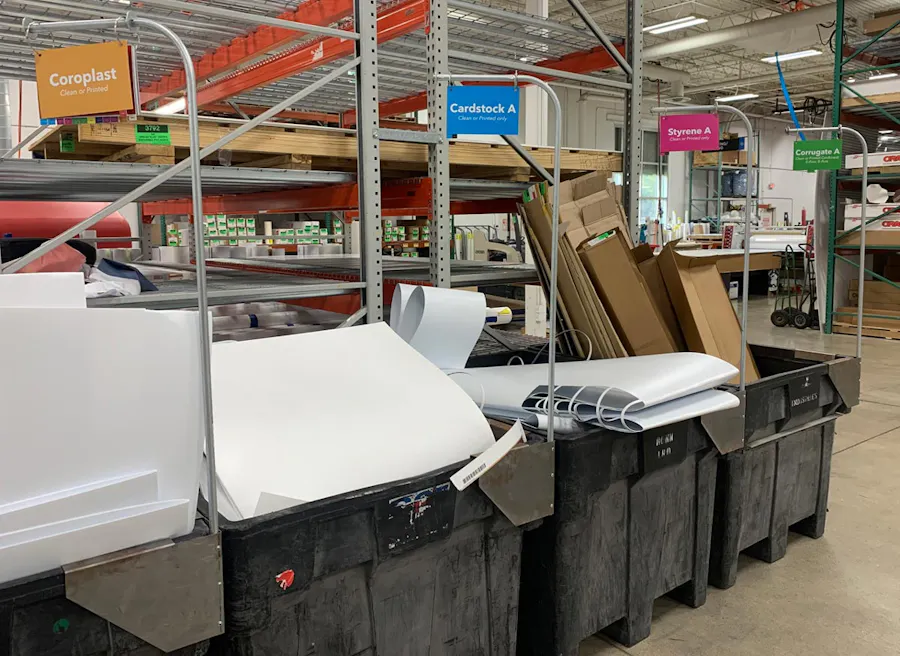 A recycling system in a production facility with four bins with labels for various materials.