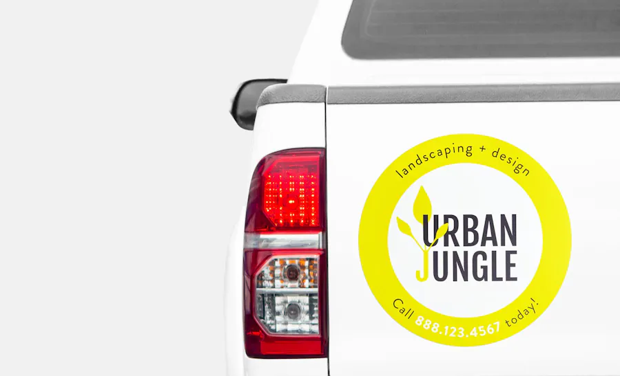 A custom car magnet on a white truck's tailgate printed with Urban Jungle Landscaping in the middle and a yellow border.