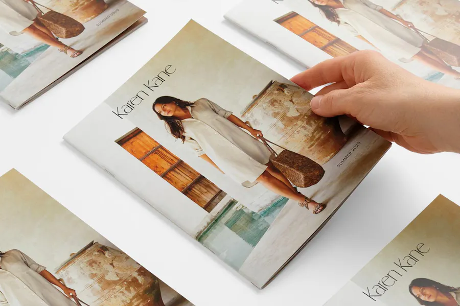 A hand laying down a summer product catalog with a saddle stitch binding and a woman in a cream dress on the front.