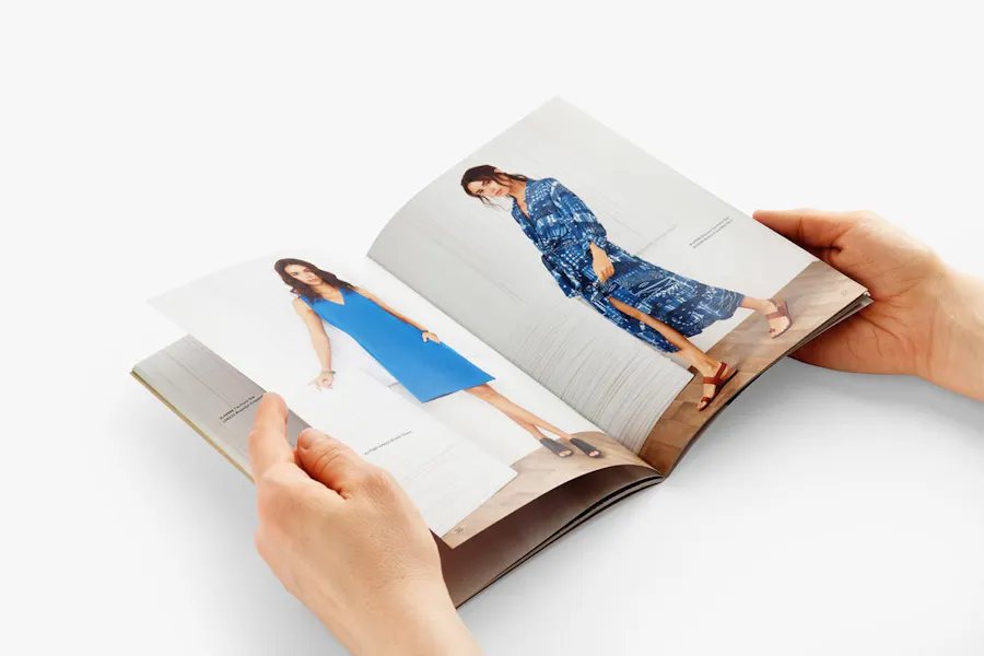 Two hands holding open a product catalog with summer marketing imagery and text.