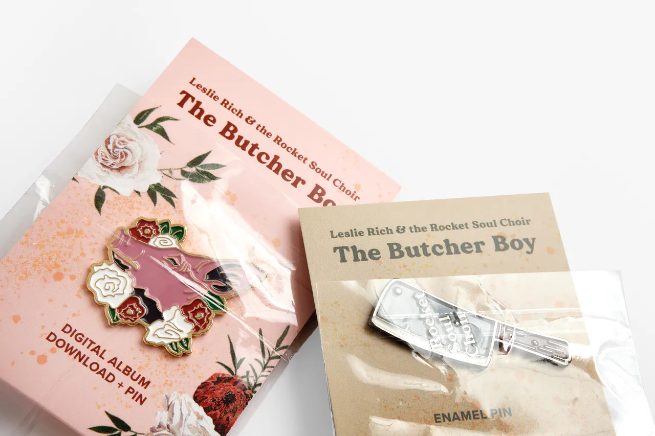 Two pins on custom backers printed with Leslie Rich & the Rocket Soul Choir in pink and tan.
