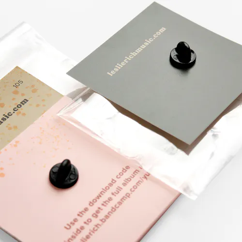 BUSINESS CARDS: BOTTOM: 120# COATED MATTE WHITE COVER, 6 X 2.4" FOLDED TO 3.5 X 2.4". TOP: 120# COATED MATTE WHITE COVER, 2.4 X 2.4" The backs of two enamel pins on custom backers printed with leslierichmusic.com.