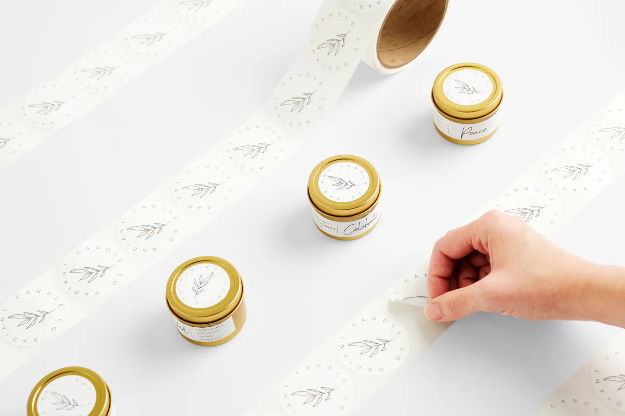 Three candles in gold jars with white labels lined up between white rolls labels printed with a leaf design.