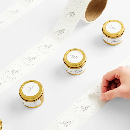 Three candles in gold jars with white labels lined up between white rolls labels printed with a leaf design.