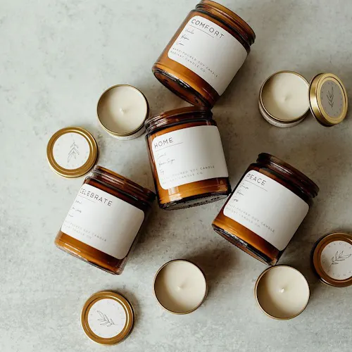 IMAGE COURTESY OF RADIANT CANDLE CO. A group of candles in jars laying on their side and candles in tins with custom printed labels on each one.