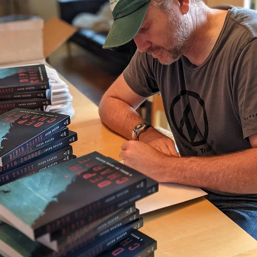 A man signing a book with two stacks of more books in front of him.