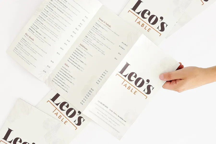 A hand holding an unfolded brochure restaurant menu with Leo's on the front and more menus above and below it.