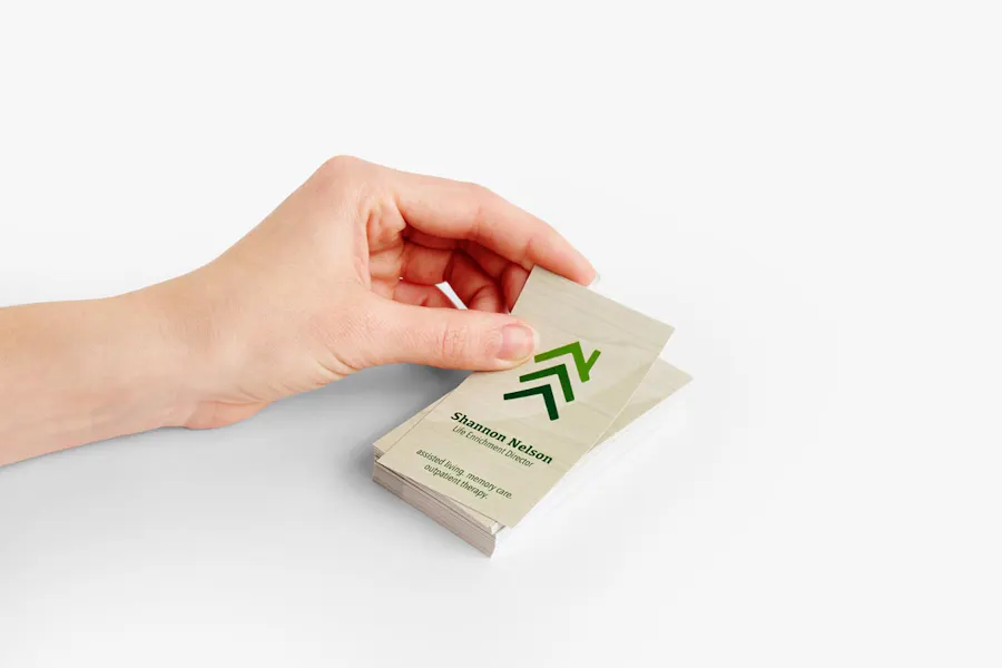 A stack of custom business cards with a tan and green design and a hand taking the one off the top.