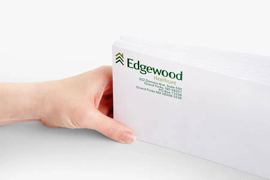 A hand holding a stack of business envelopes with the address for a senior living facility in the left corner.